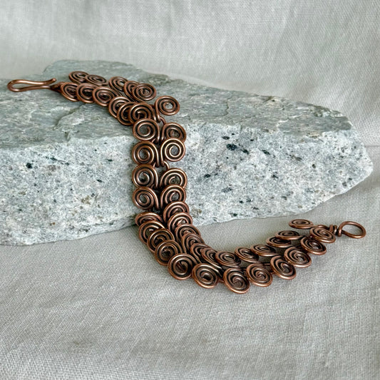 Copper bracelet with intricate spiral design on a stone and fabric background