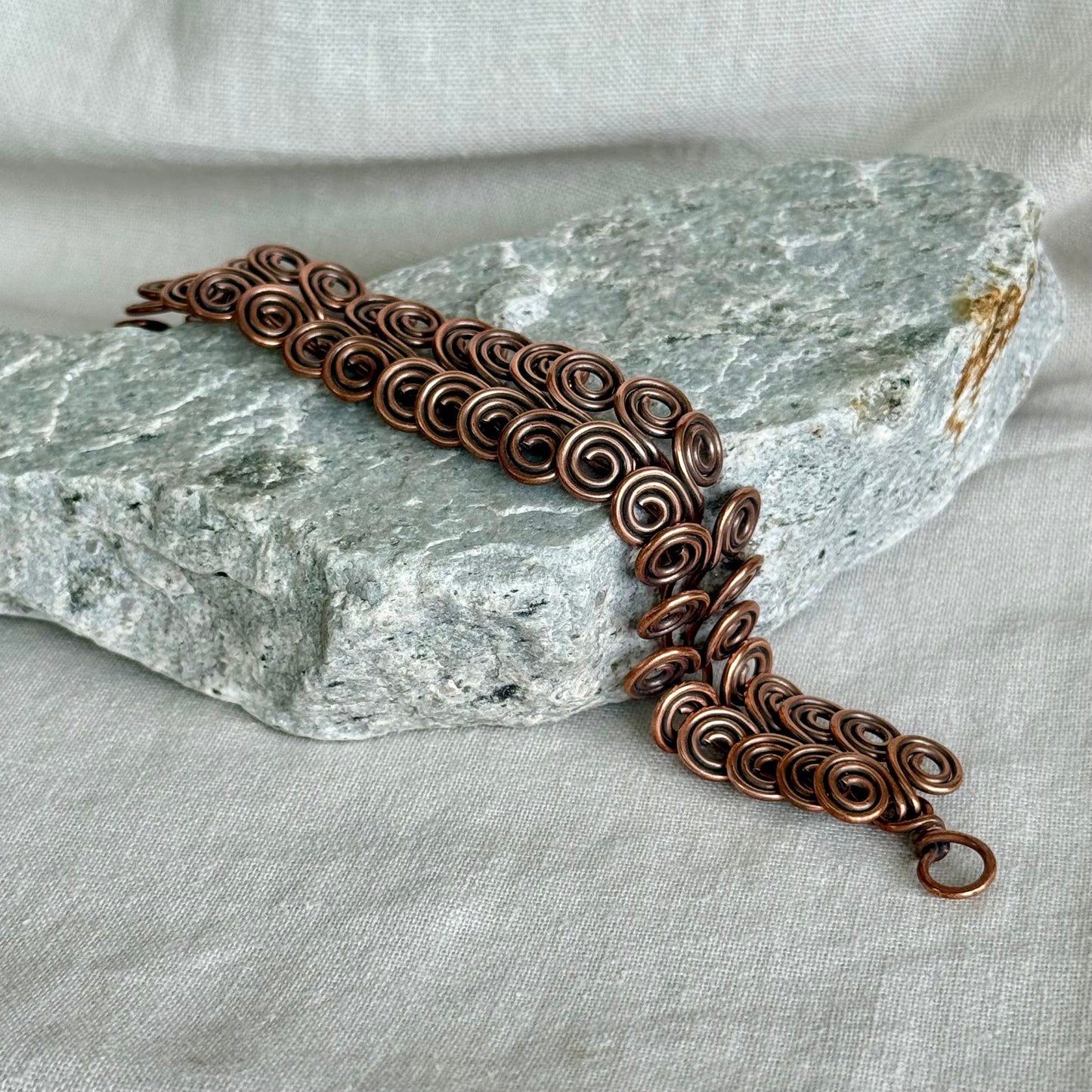Copper bracelet with intricate spiral design on a stone and fabric background