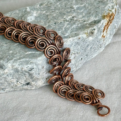 Copper bracelet with intricate spiral design on a stone and fabric background