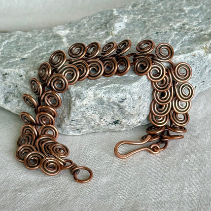 Copper bracelet with intricate spiral design on a stone and fabric background