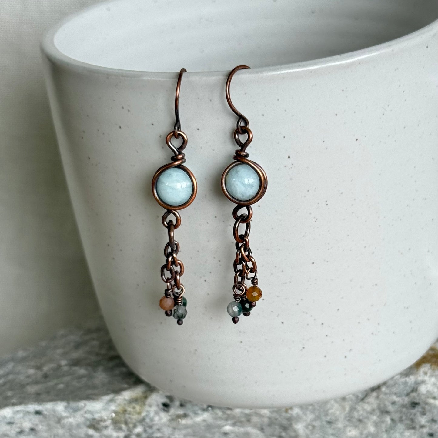 Pair of copper earrings with blue gemstones and copper accents hanging over a white ceramic bowl.