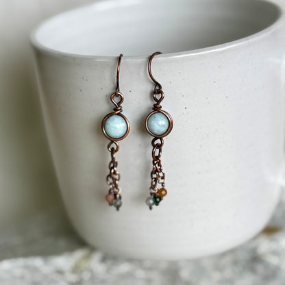 Pair of copper earrings with turquoise stones and chain details on a white ceramic cup.