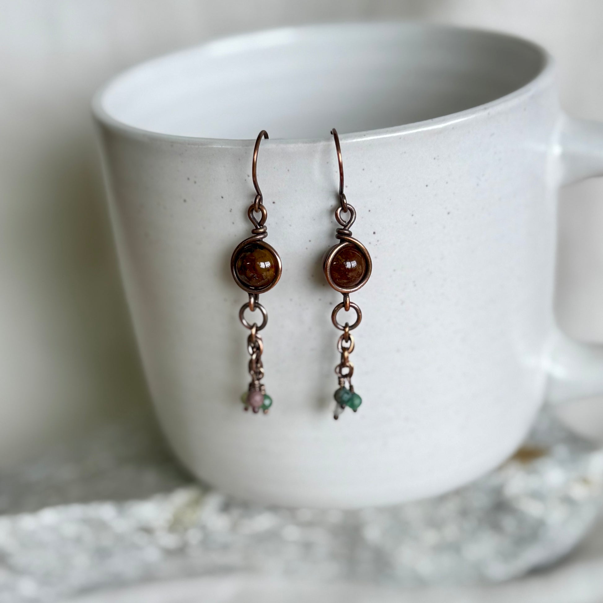 Pair of copper earrings with gemstones on a white mug