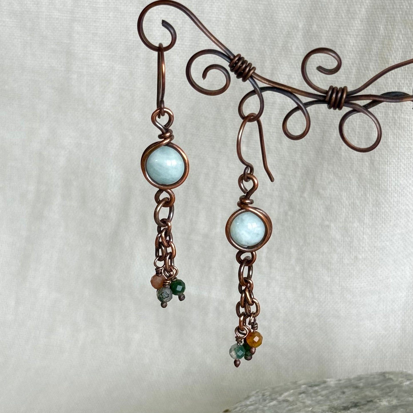 Pair of copper earrings with light blue gemstones on a white background
