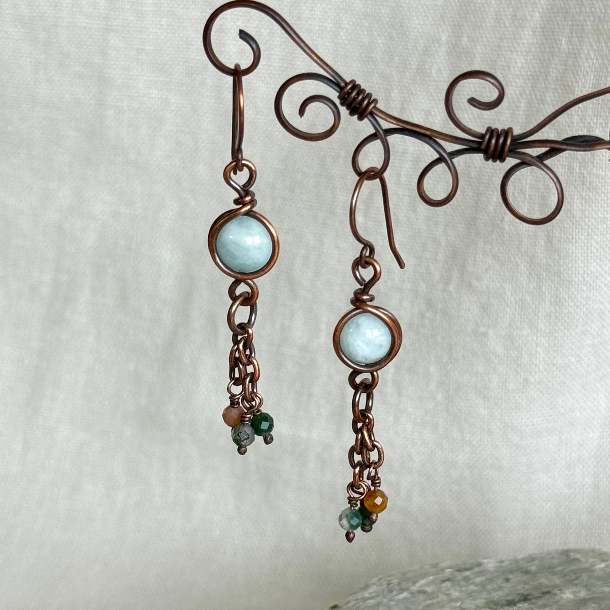 Pair of copper earrings with light blue gemstones on a white background