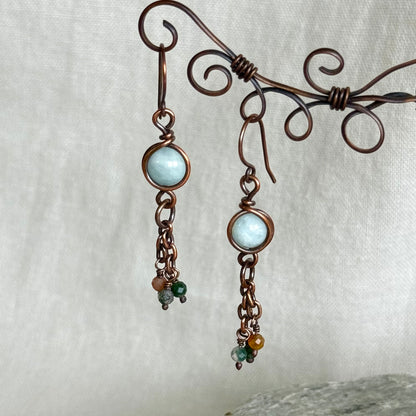 Pair of copper earrings with light blue gemstones on a white background