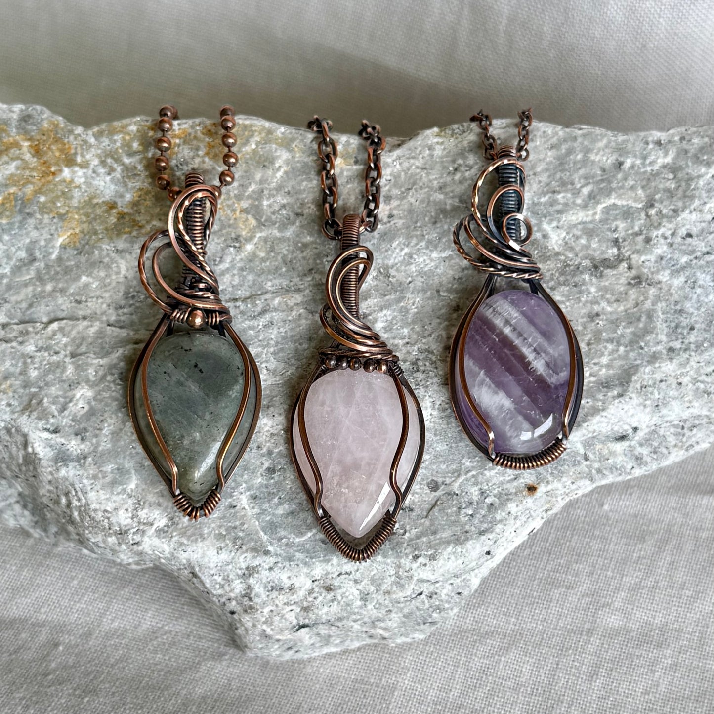 Copper pendant with purple stones and a black cord on a piece of stone on linen background