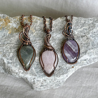 Copper pendant with purple stones and a black cord on a piece of stone on linen background