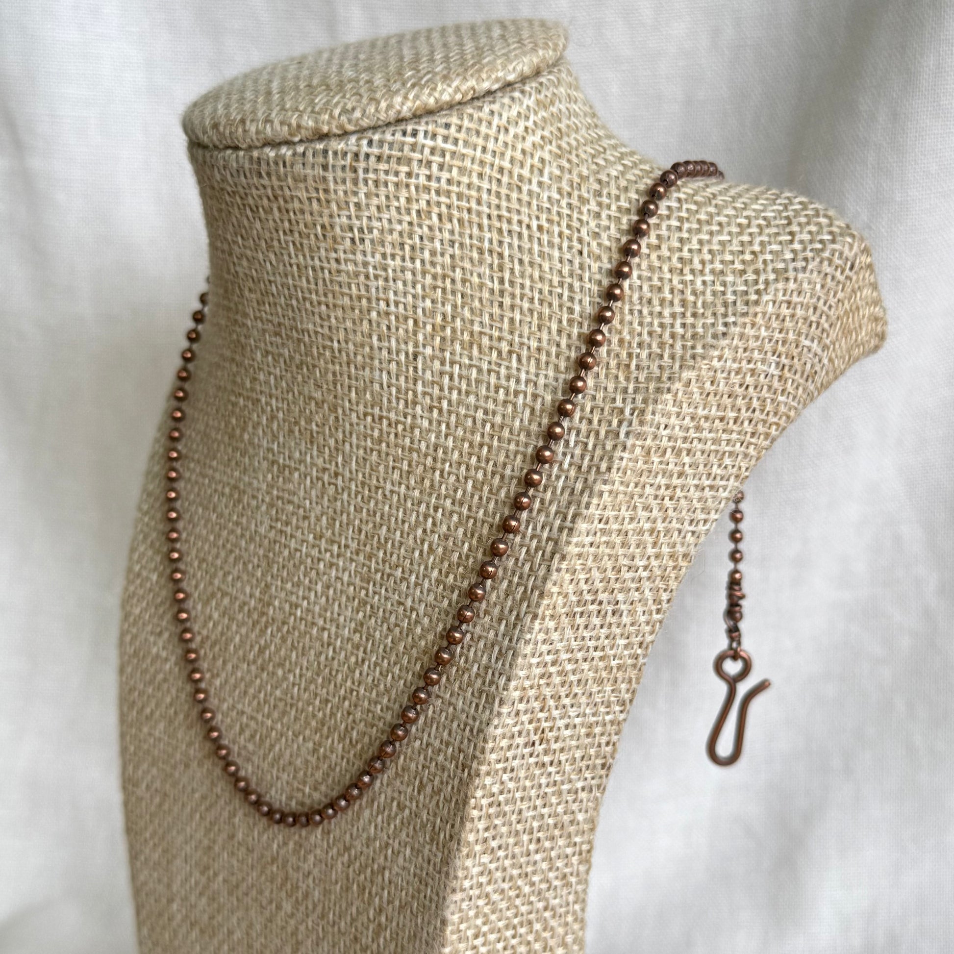 Copper ball chain necklace on a beige mannequin bust with a white background