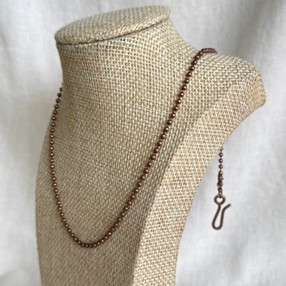 Copper ball chain necklace on a beige mannequin bust with a white background