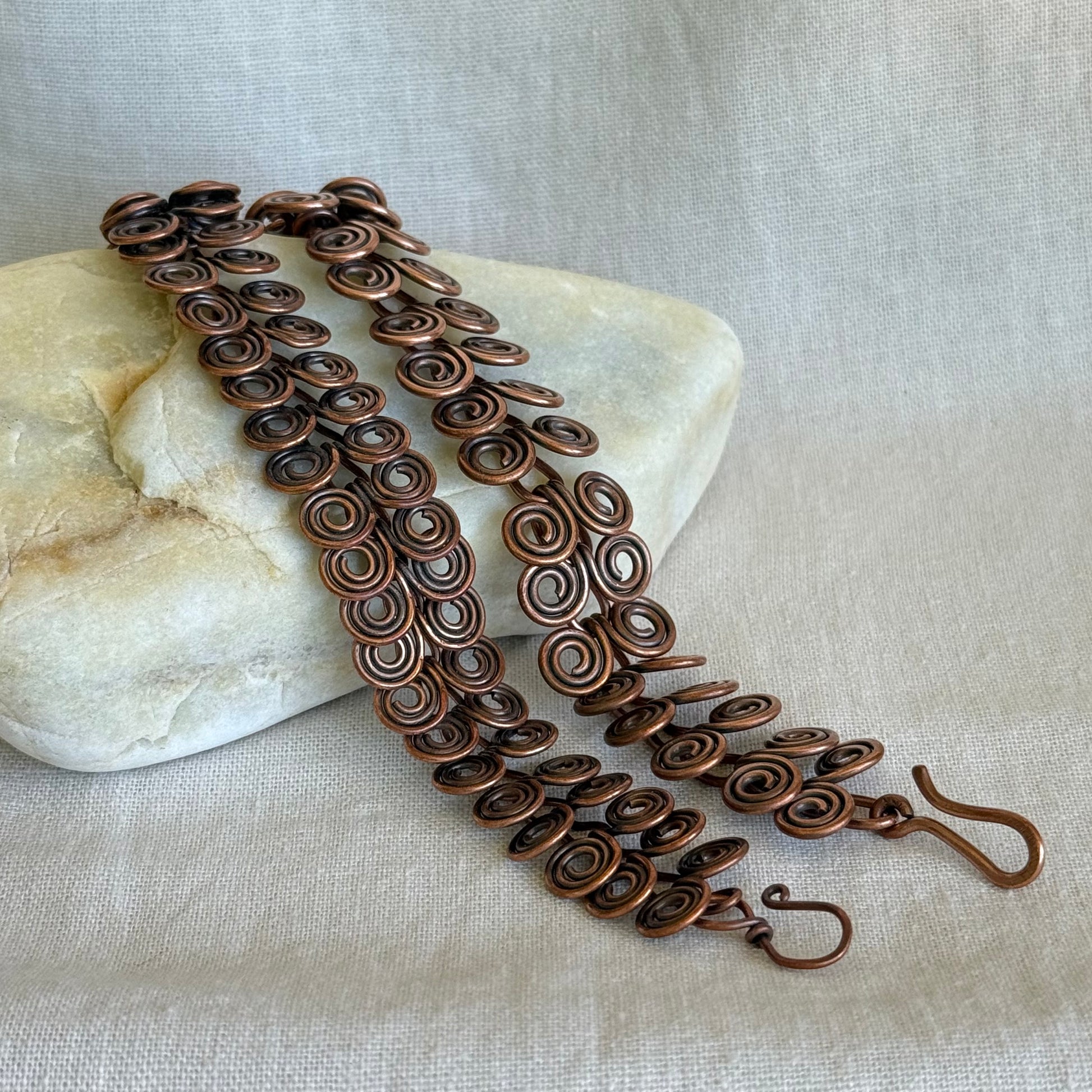 two Copper bracelets with intricate spiral design on a stone with a beige fabric background