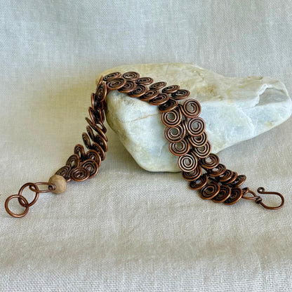 Copper bracelet with intricate spiral design on a stone with a beige fabric background
