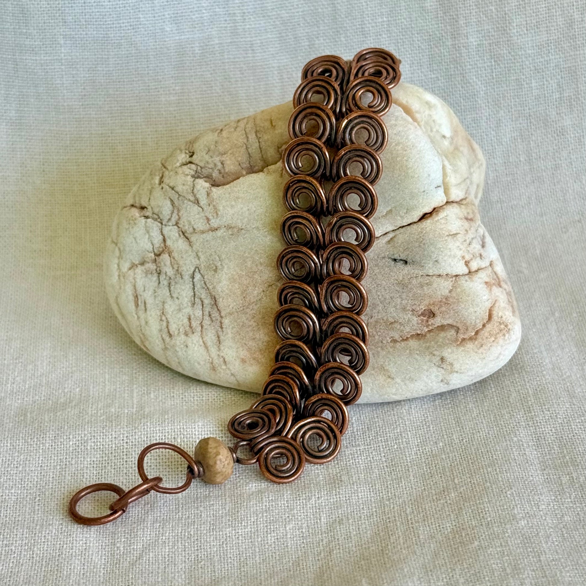 Copper bracelet with intricate spiral design on a stone with a beige fabric background