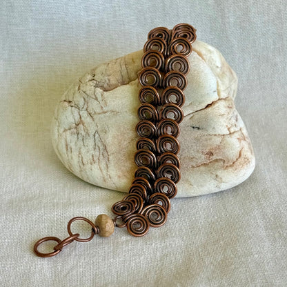 Copper bracelet with intricate spiral design on a stone with a beige fabric background