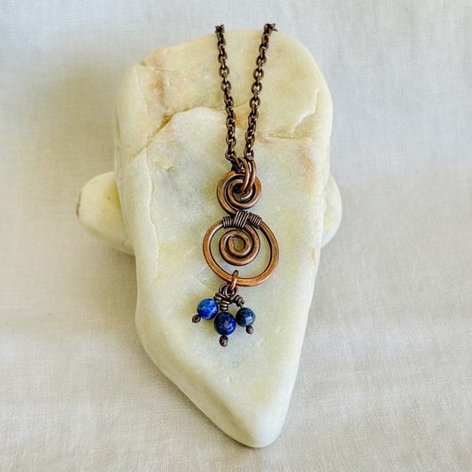 Necklace with a copper spiral pendant and blue beads on a stone surface