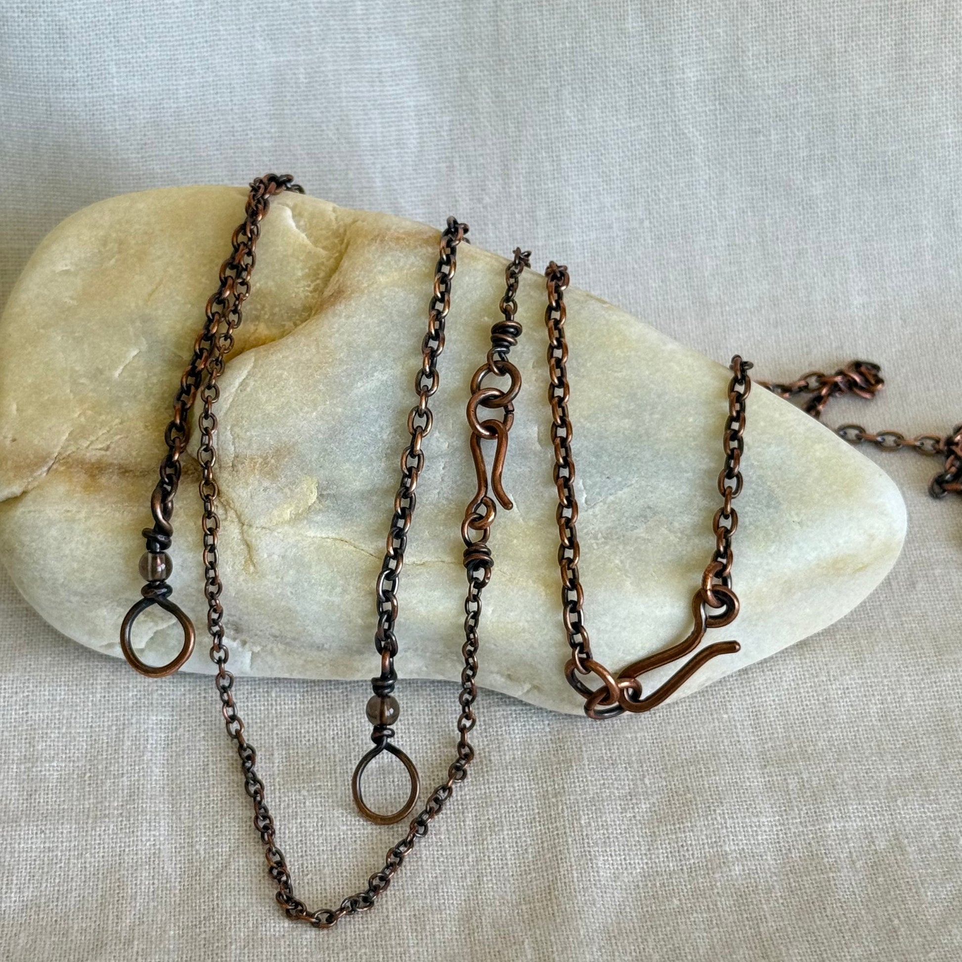 Four handmade copper chain necklaces on a stone surface