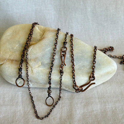 Four handmade copper chain necklaces on a stone surface