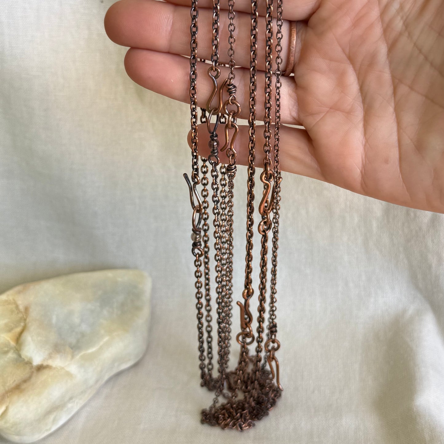 Hand holding six handmade copper chains on a light background
