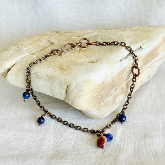Copper chain bracelet or anklet with blue and red beads on a stone surface