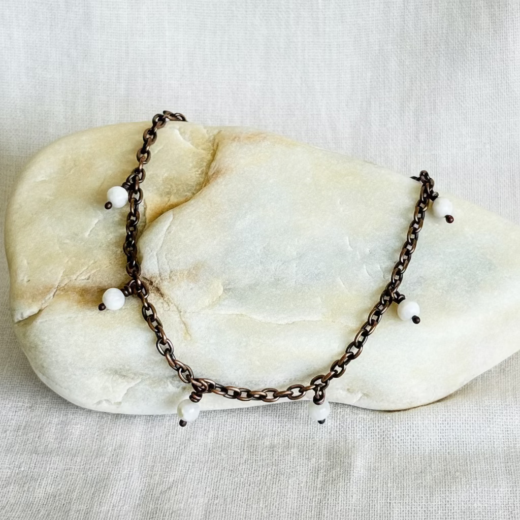 copper anklet with white beads on a stone surface