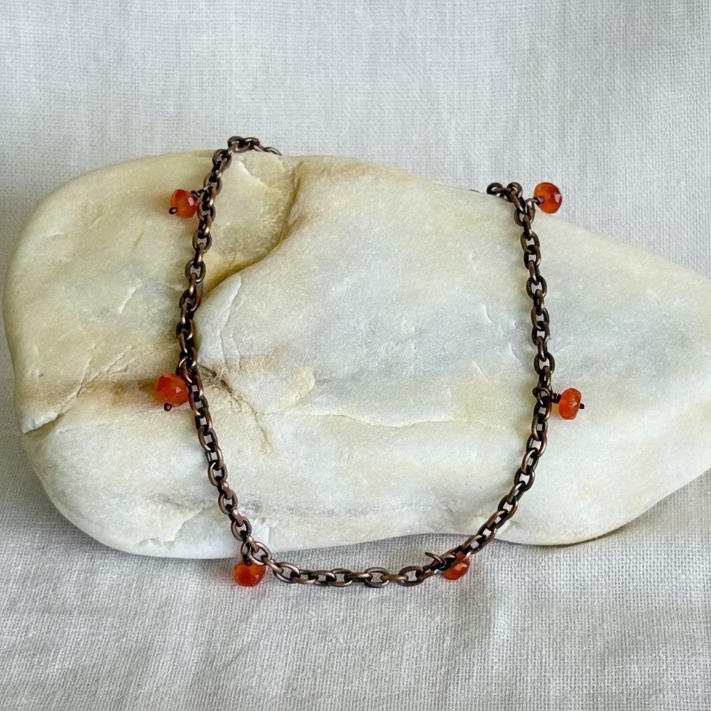 copper anklet with orange beads on a stone surface