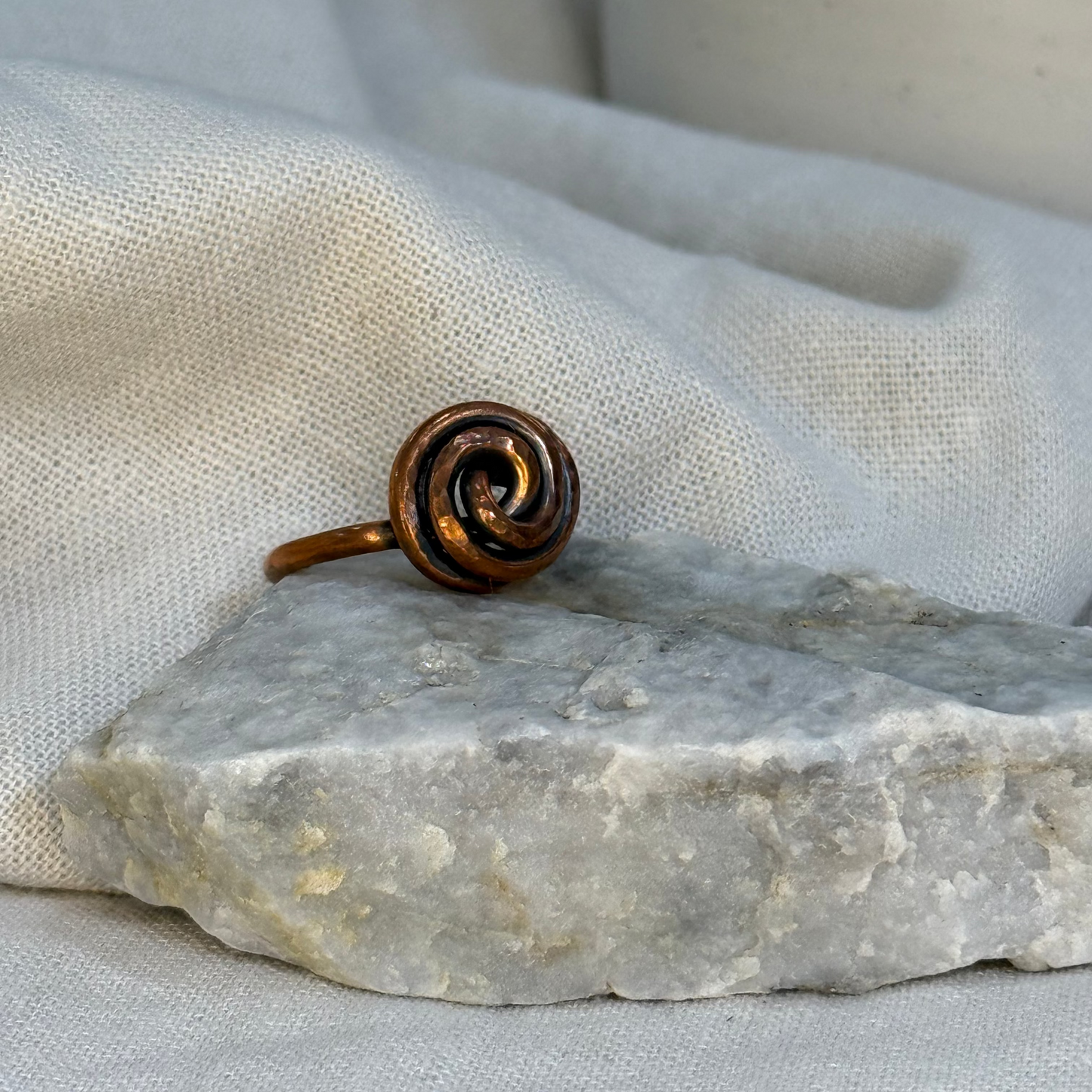 Copper spiral ring on a white grey stone with linen fabric background