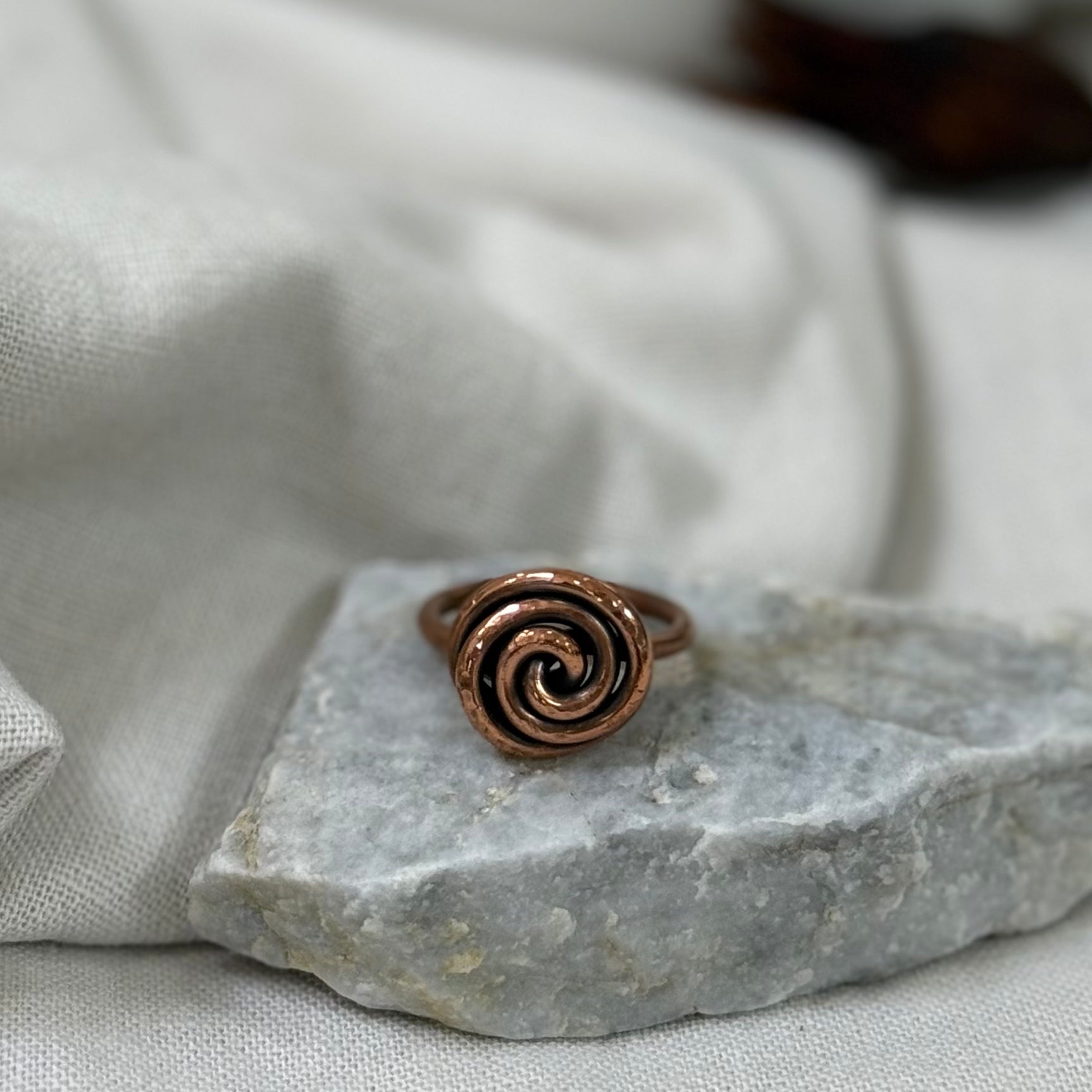 Copper spiral ring on a white grey stone with linen fabric background