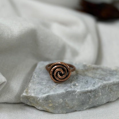 Copper spiral ring on a white grey stone with linen fabric background
