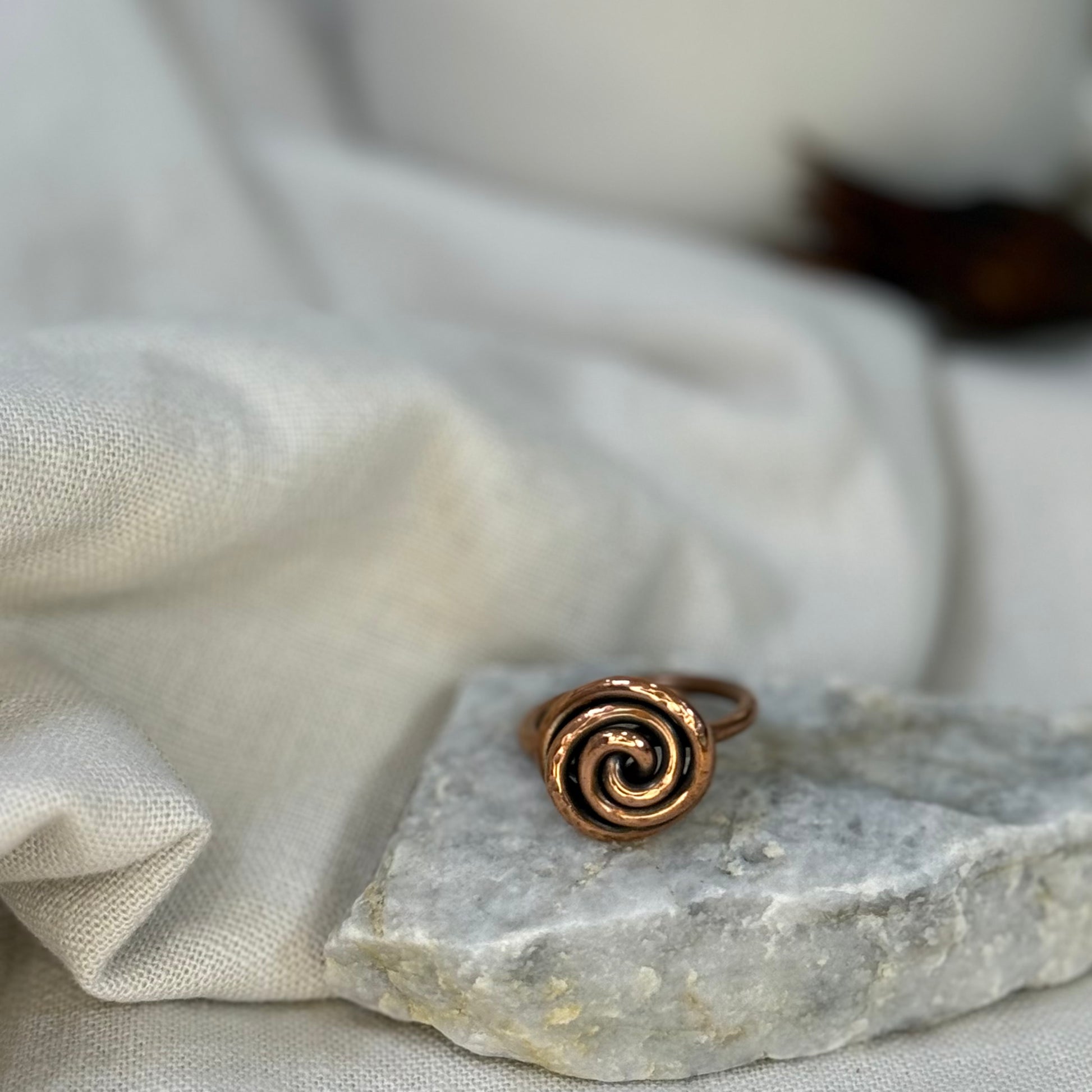 Copper spiral ring on a white grey stone with linen fabric background