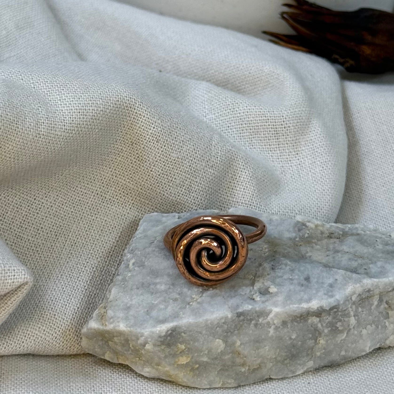 Copper spiral ring on a white grey stone with linen fabric background