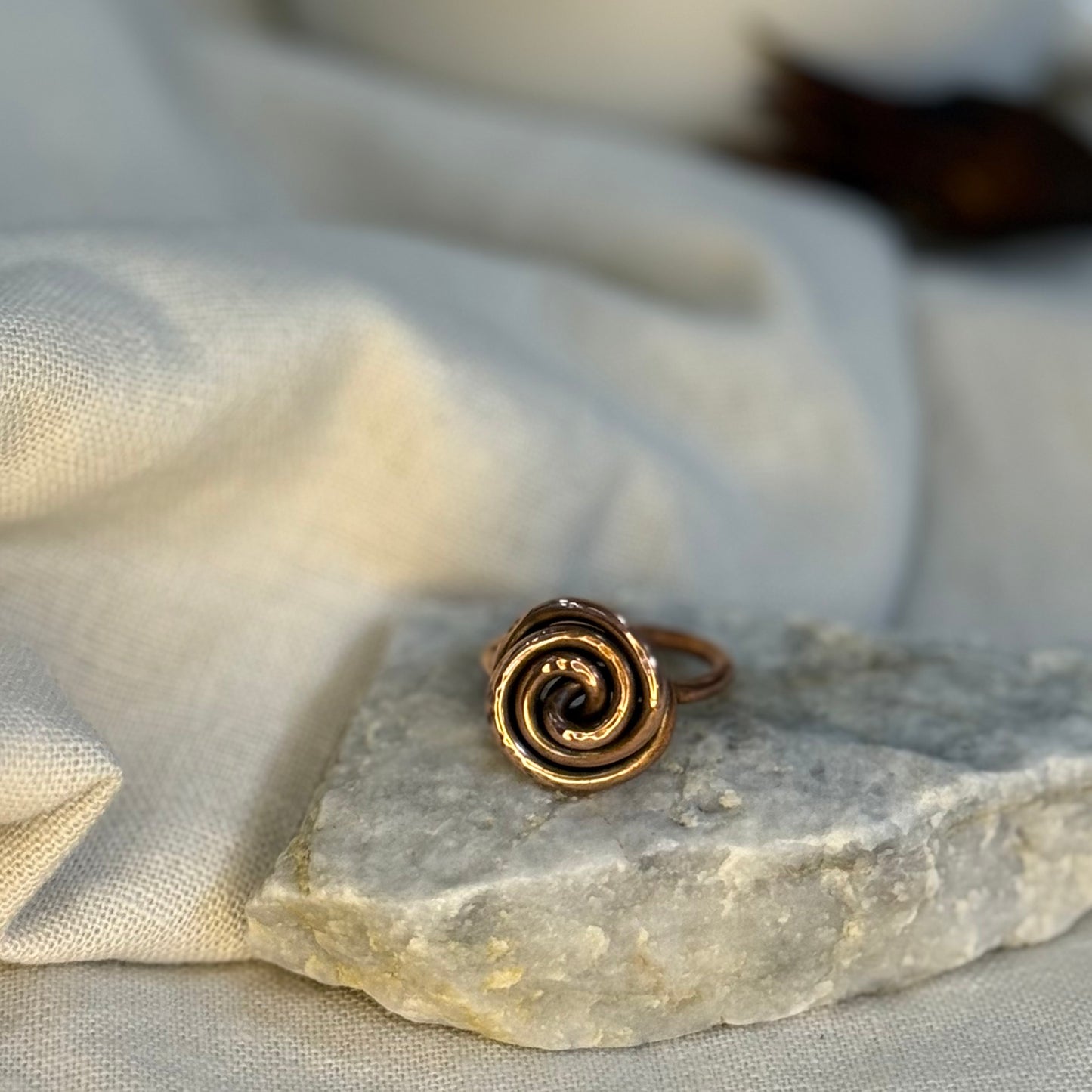 Copper spiral ring on a white grey stone with linen fabric background