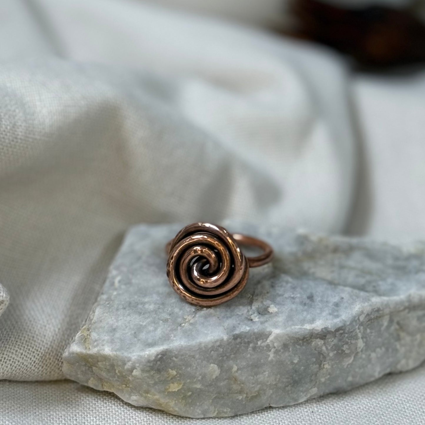 Copper spiral ring on a white grey stone with linen fabric background