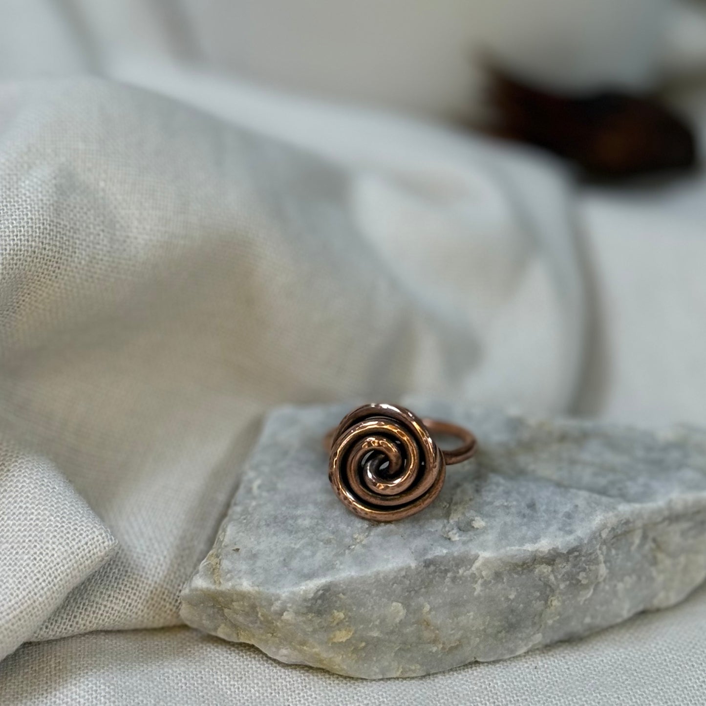 Copper spiral ring on a white grey stone with linen fabric background