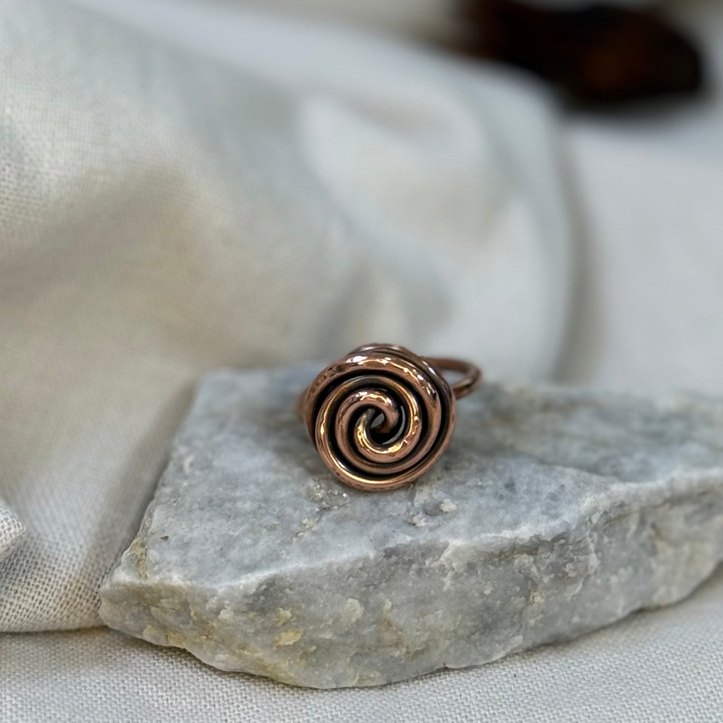 Copper spiral ring on a white grey stone with linen fabric background