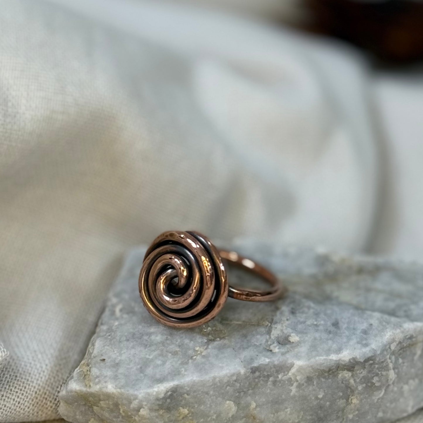 Copper spiral ring on a white grey stone with linen fabric background