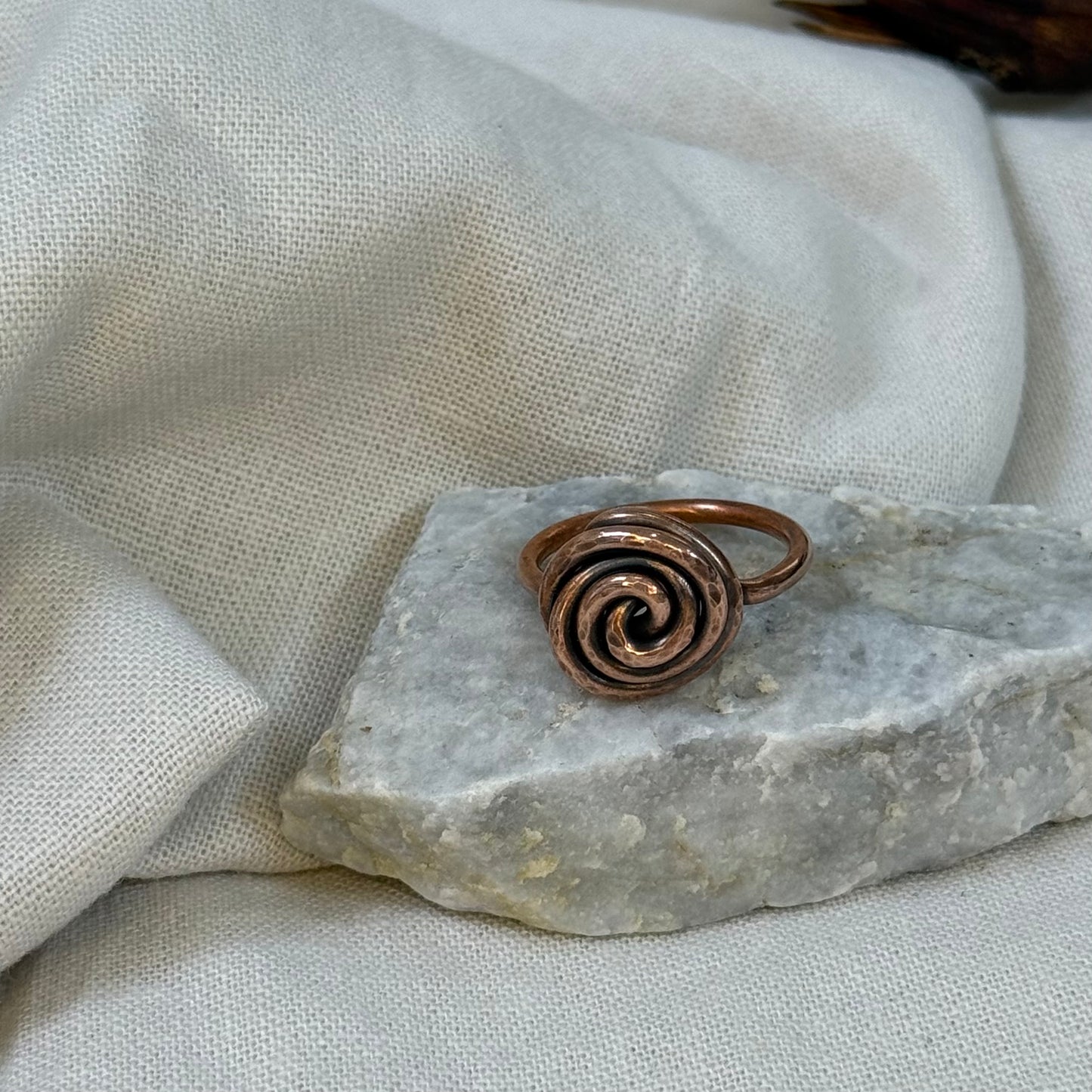 Copper spiral ring on a white grey stone with linen fabric background