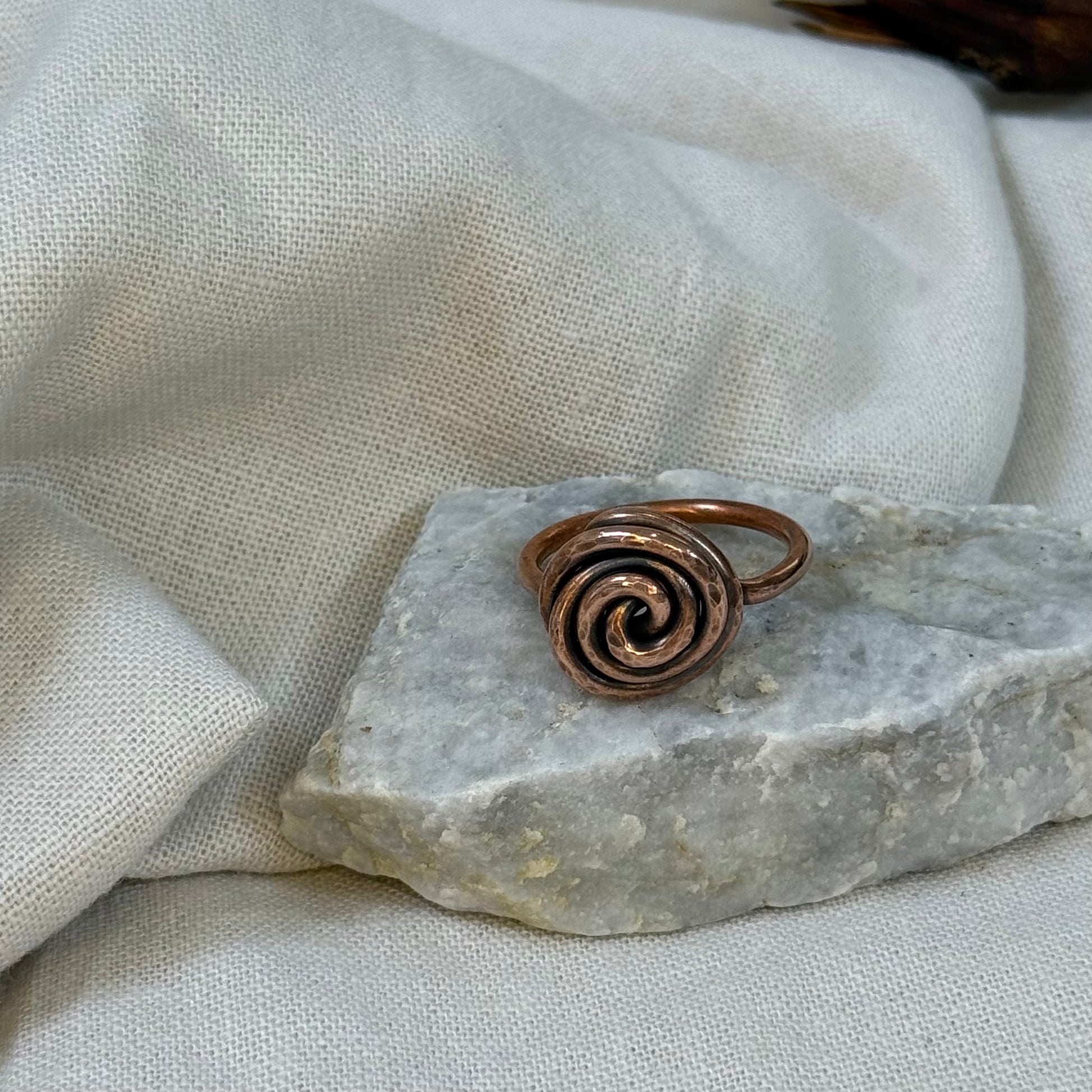 Copper spiral ring on a white grey stone with linen fabric background