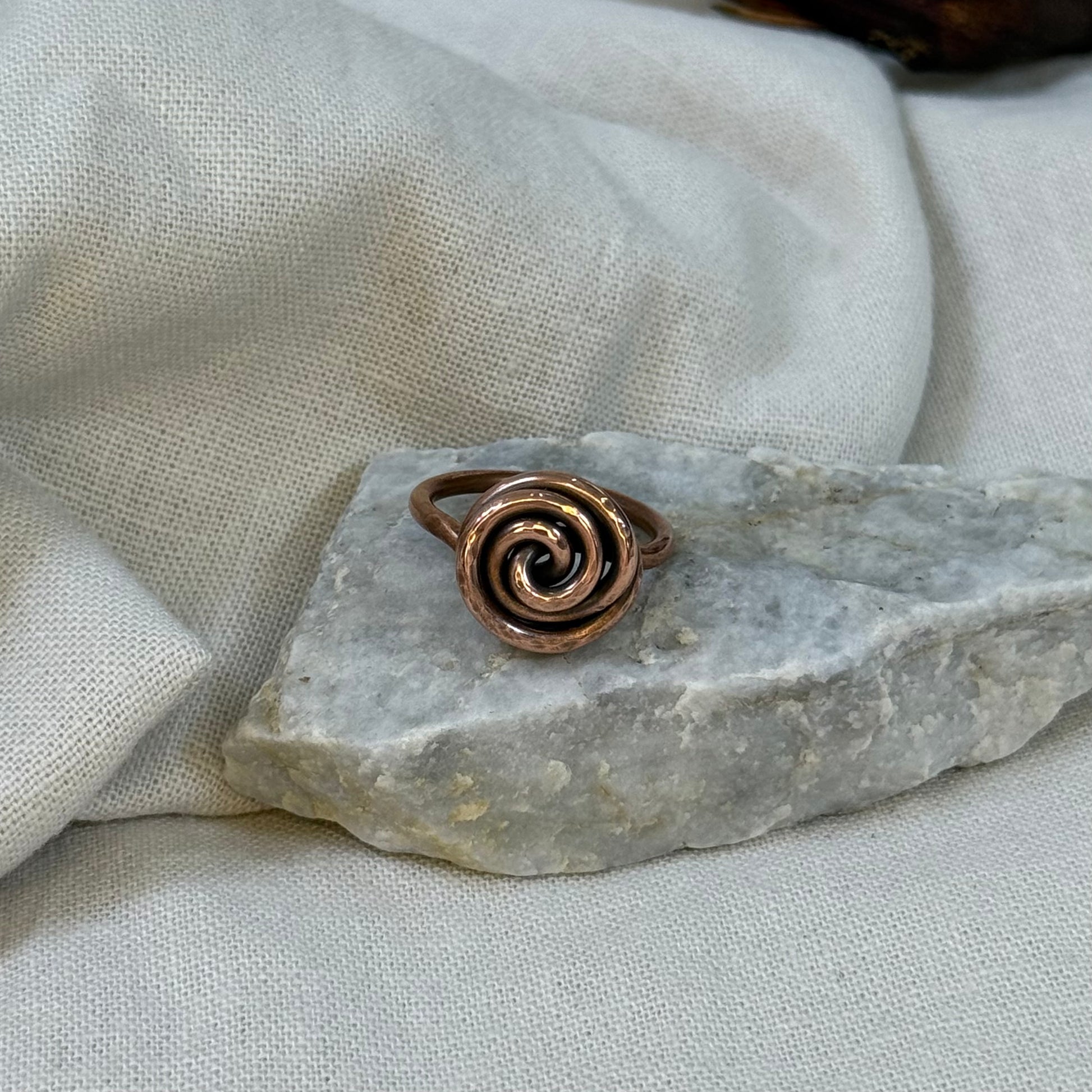 Copper spiral ring on a white grey stone with linen fabric background
