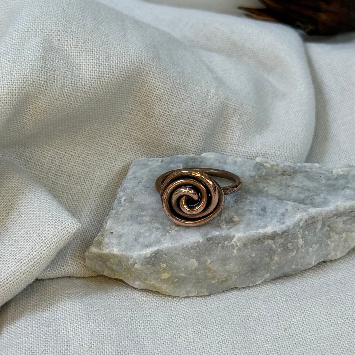 Copper spiral ring on a white grey stone with linen fabric background