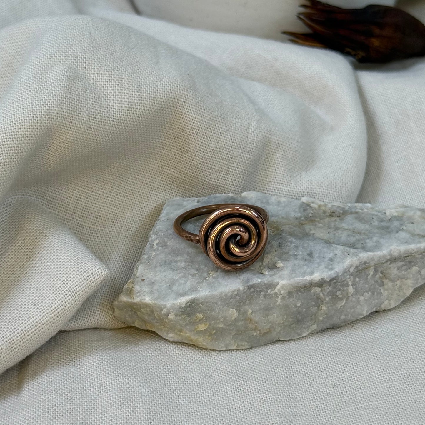 Copper spiral ring on a white grey stone with linen fabric background