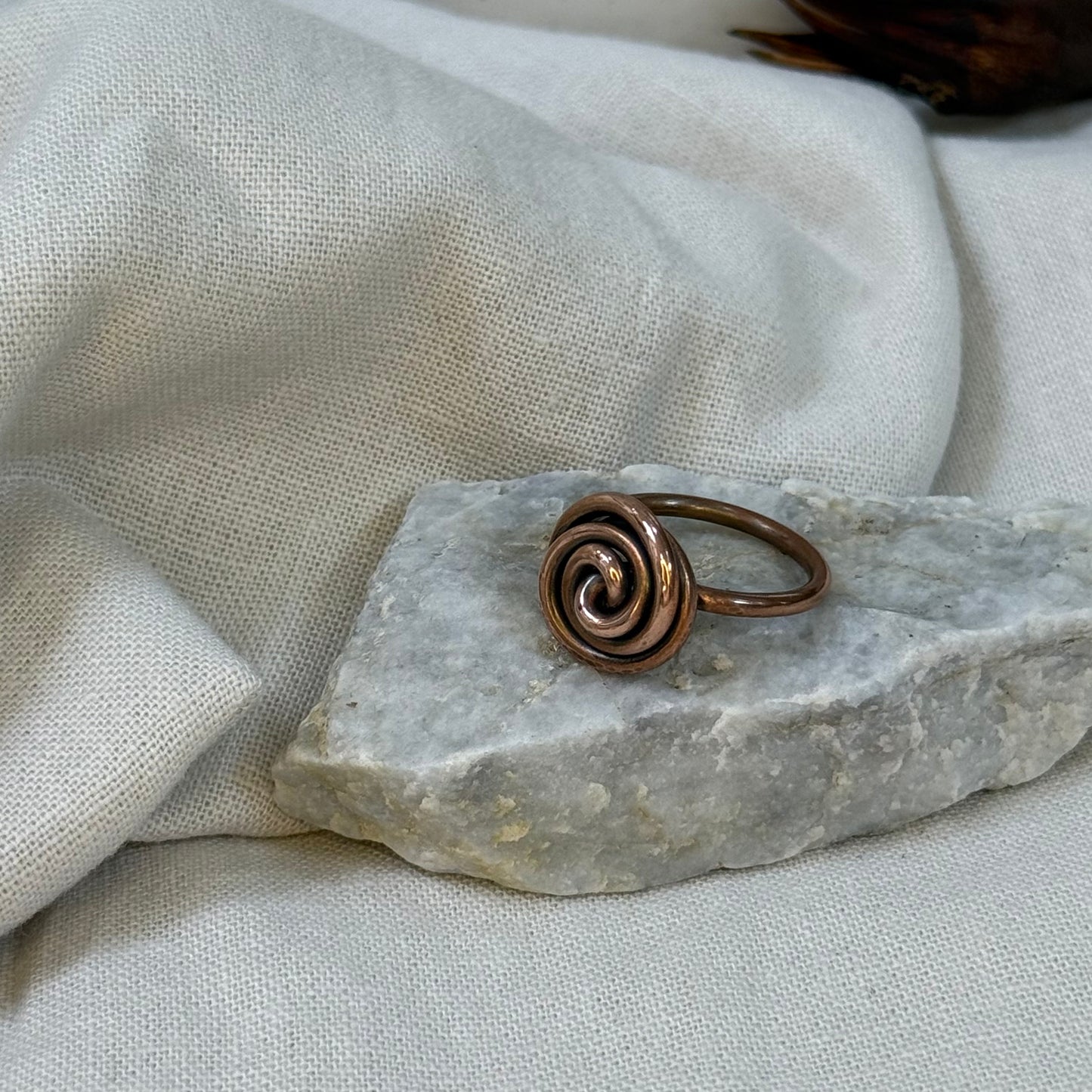 Copper spiral ring on a white grey stone with linen fabric background