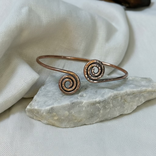 Copper bangle with spiral design on a stone surface with linen background