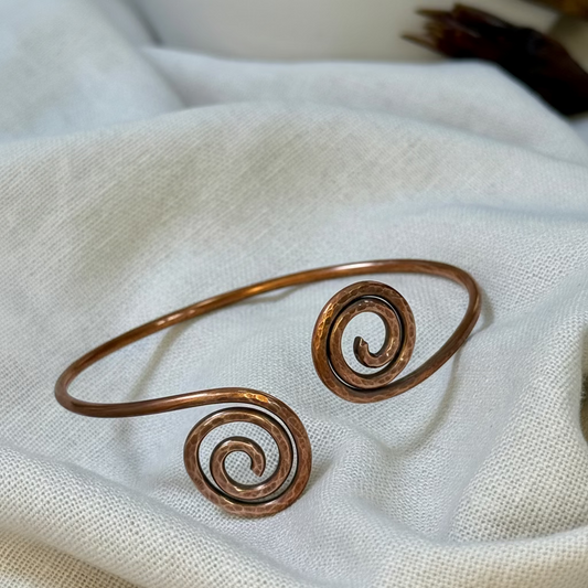 Copper bangle with spiral design on a linen background