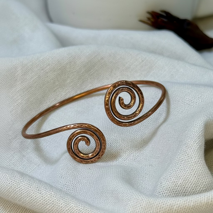 Copper bangle with spiral design on a  linen background
