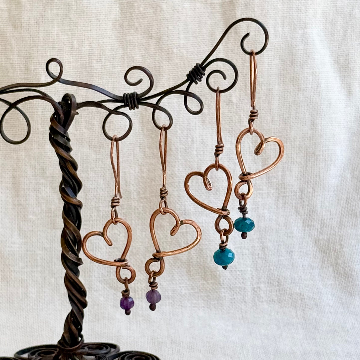 Heart-shaped copper earrings with beads on a decorative stand against a beige background