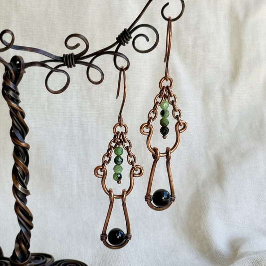 Pair of copper earrings with green and black beads on a decorative stand.