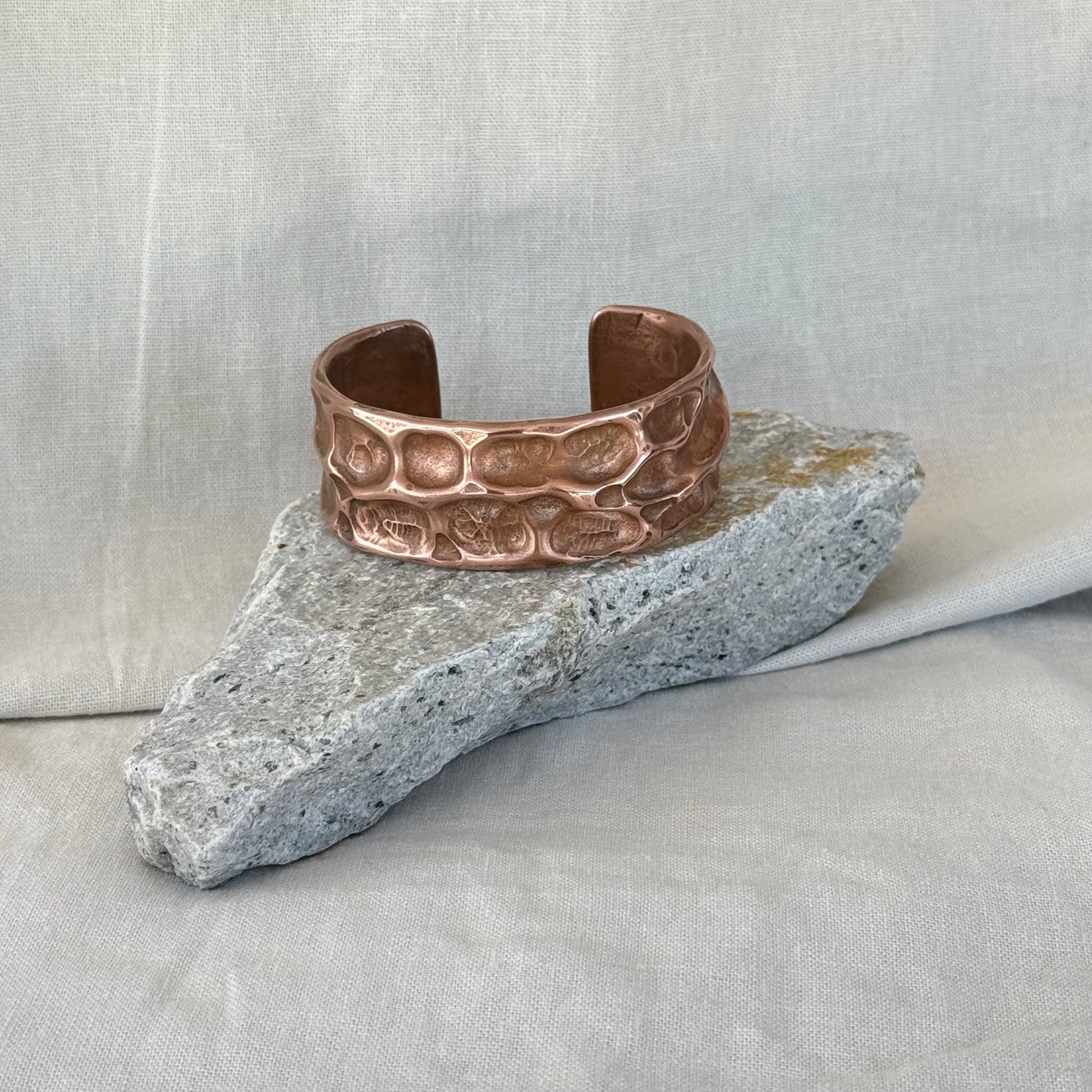 Copper cuff with hammered, textured design on a stone surface with linen background