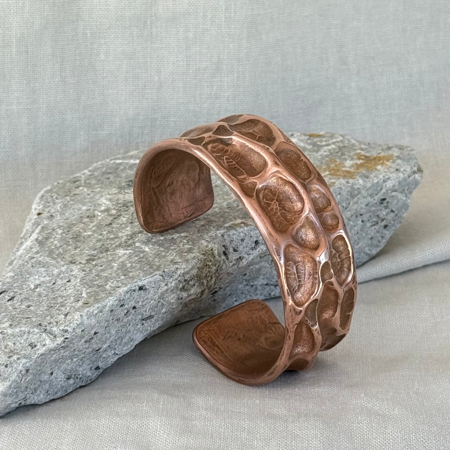 Copper cuff with hammered, textured design on a stone surface with linen background