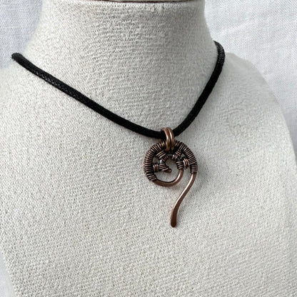 A handmade necklace featuring a textured copper spiral pendant on a black cord, displayed on a textured white fabric mannequin bust.