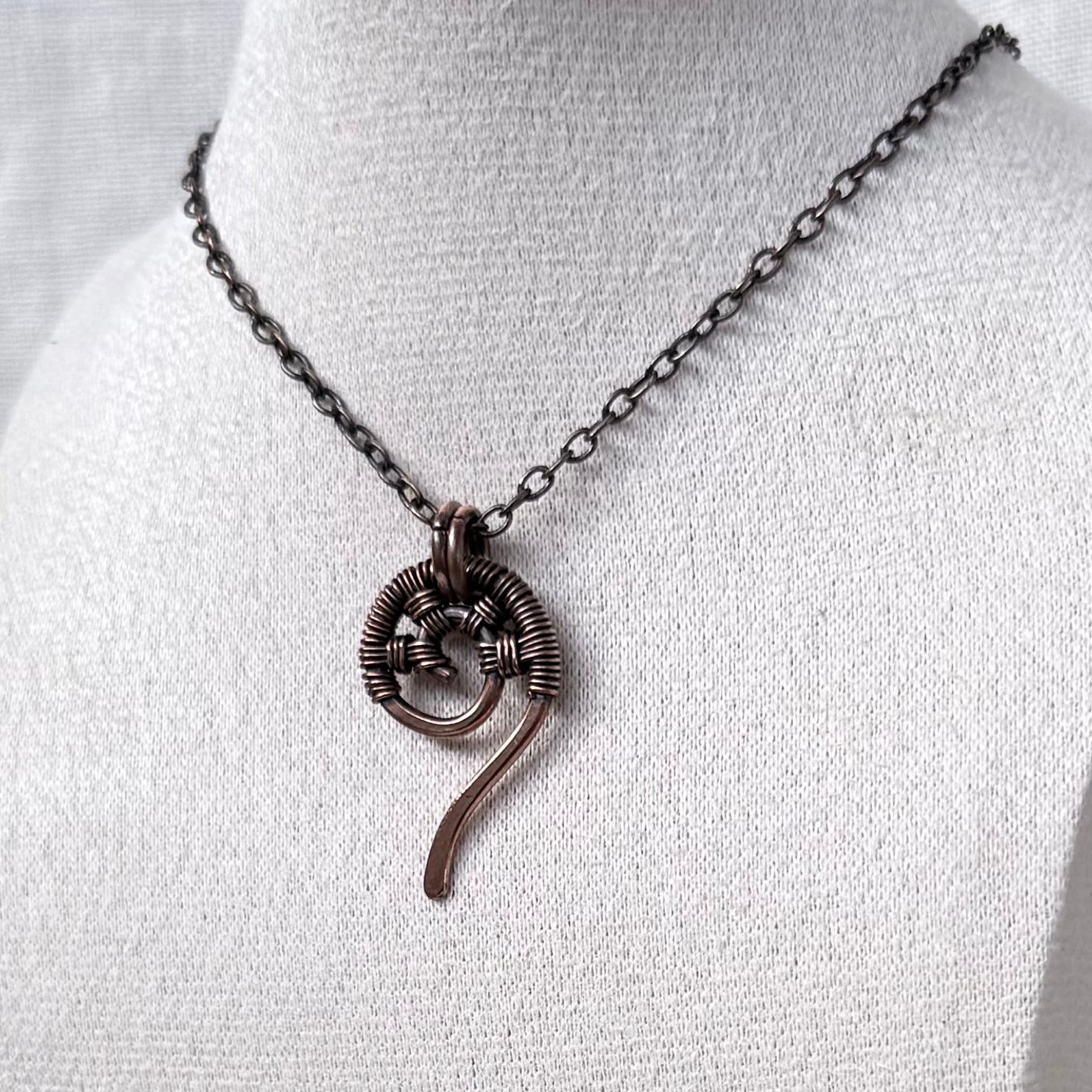 A dark copper wire-wrapped spiral pendant necklace displayed on a white fabric jewellery bust.